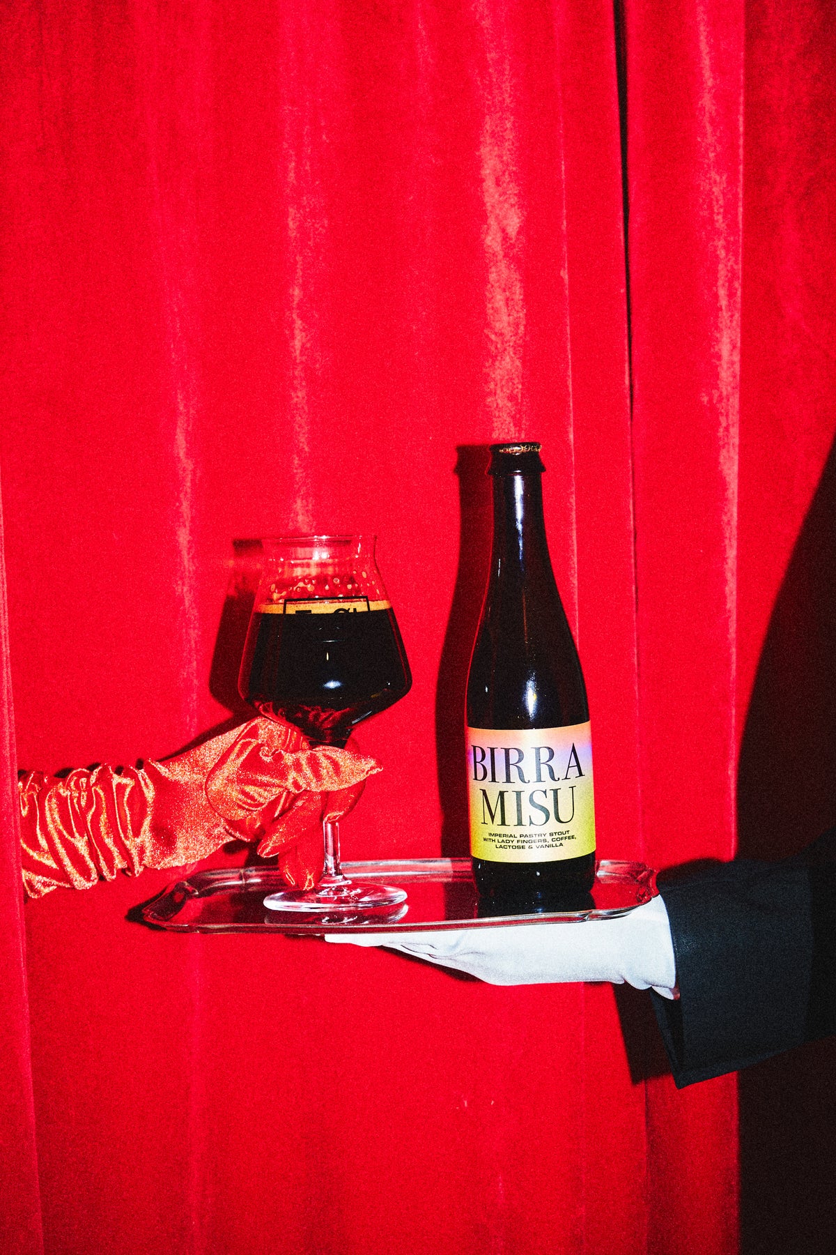 Birramisu bottle by To Øl poured in a pint glass with dark beer and red background.
