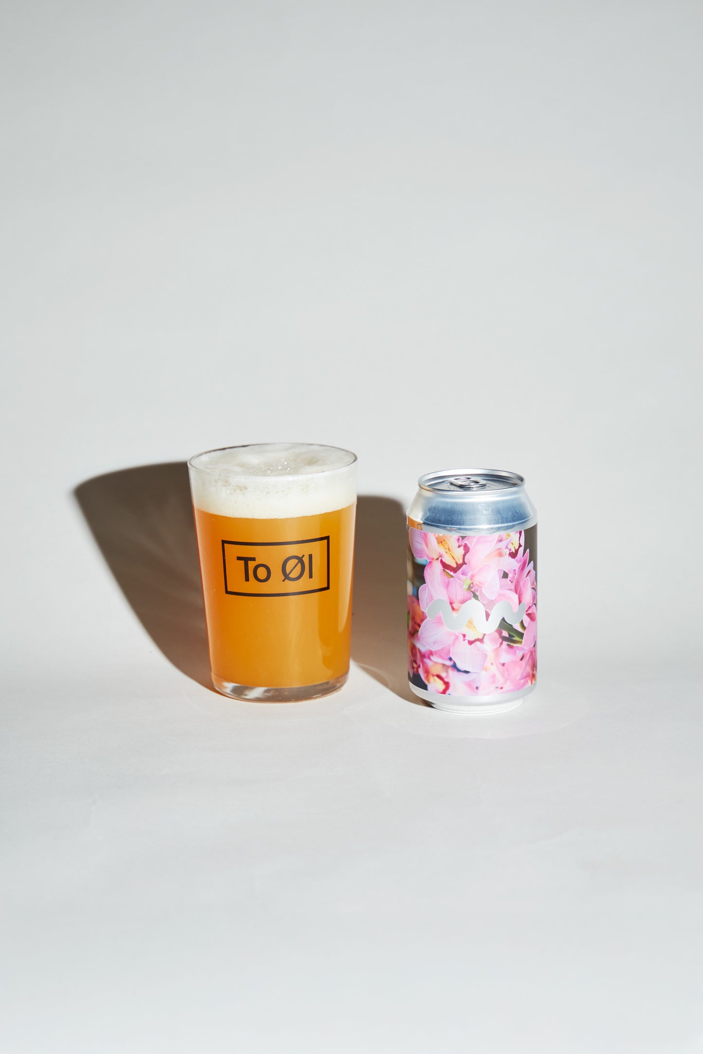 Glass of beer with a floral-patterned can of Tropical Rumble on a white background