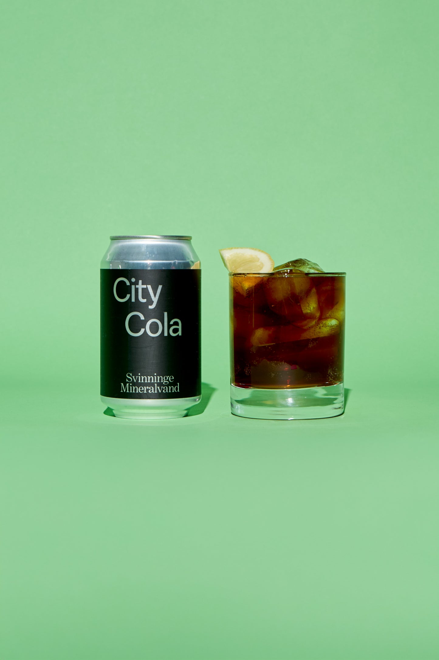 City Cola silver and black can and glass with cola on a green background