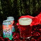 Two cans of 45 Days of X-mas poured in a To Øl beer glass featuring a Christmas setting background.