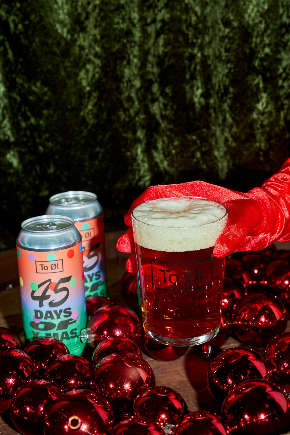 Two cans of 45 Days of X-mas poured in a To Øl beer glass featuring a Christmas setting background.
