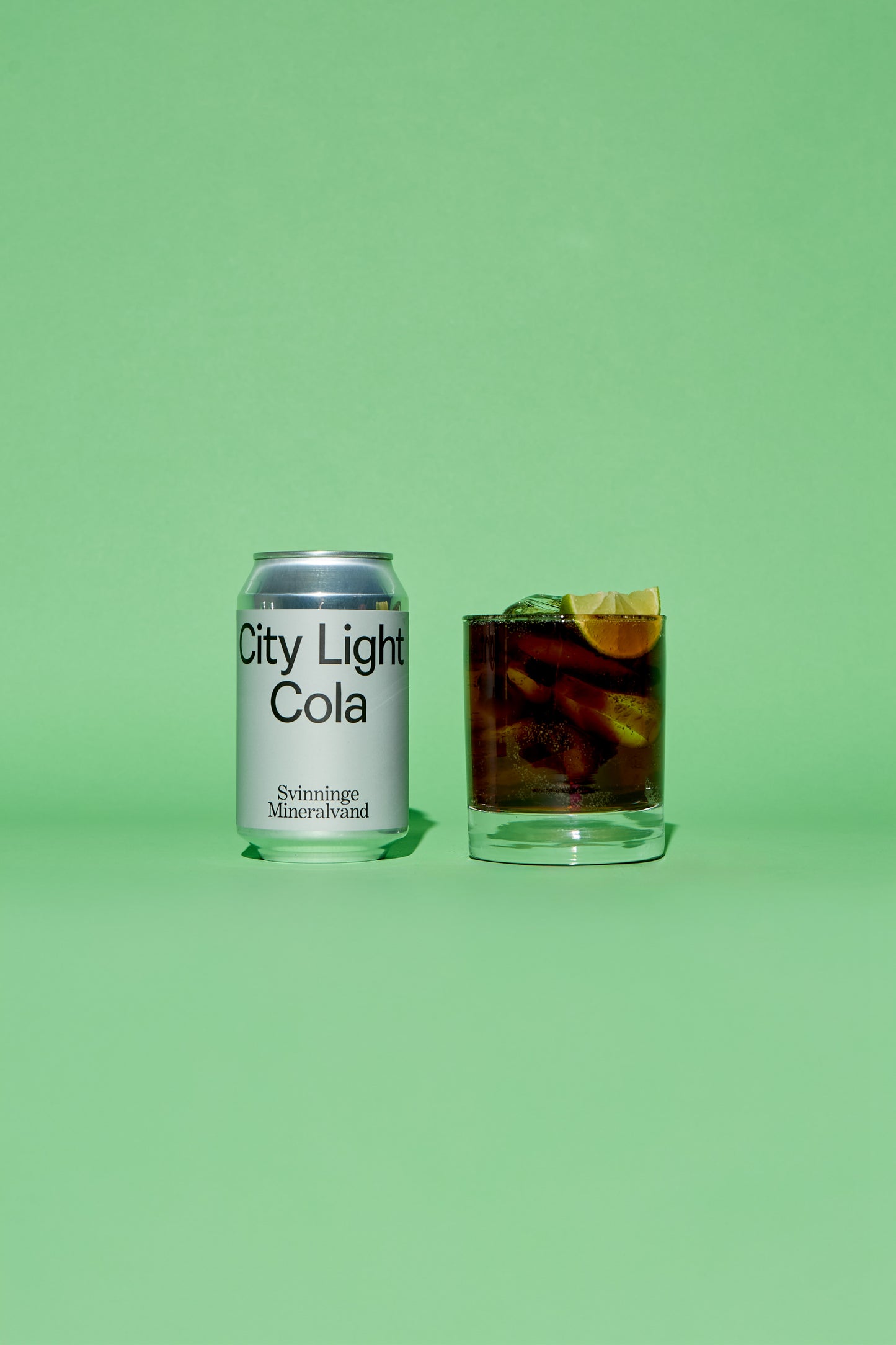 City Light Cola silver grey can and glass with drink on a green background