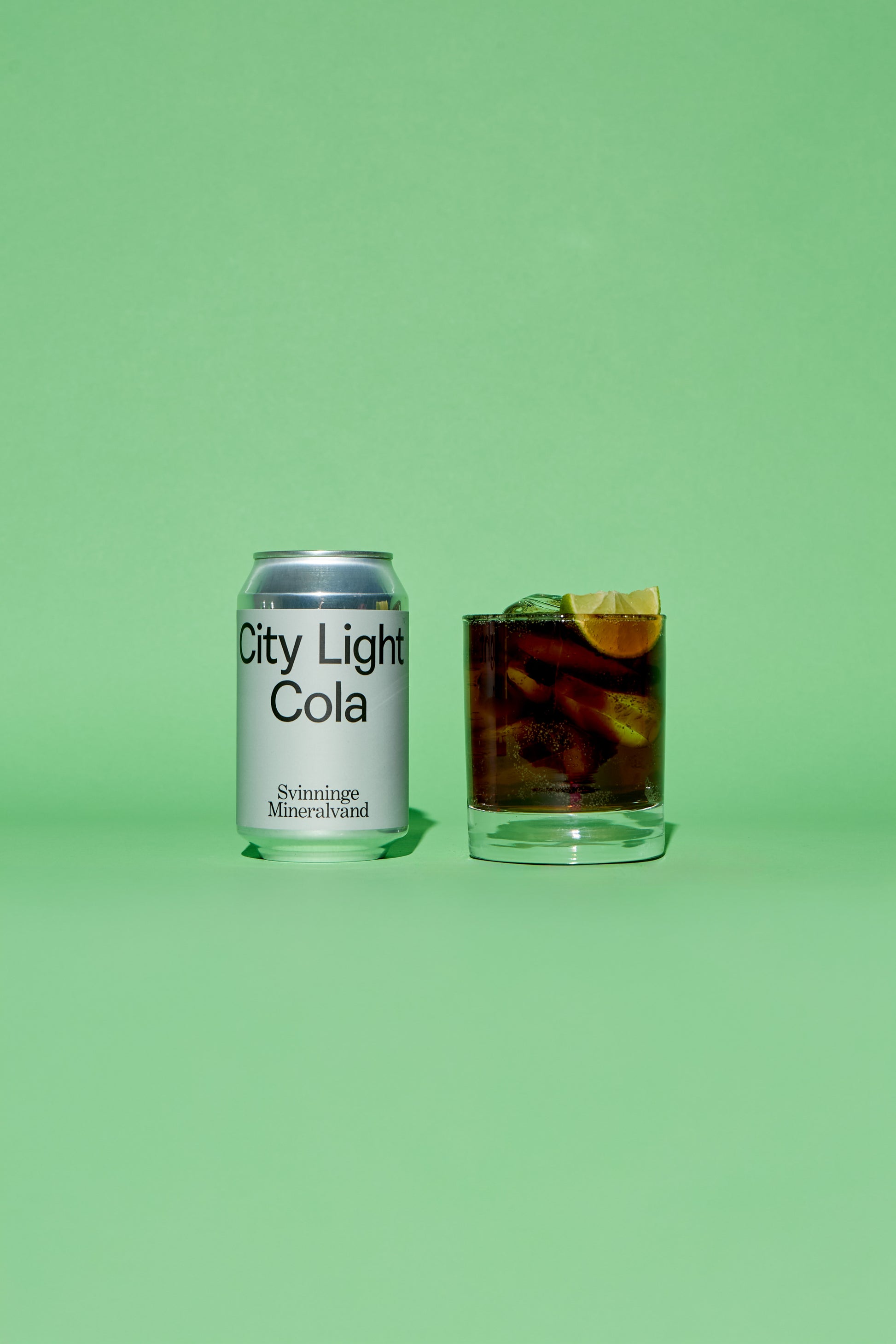 City Light Cola silver grey can and glass with drink on a green background