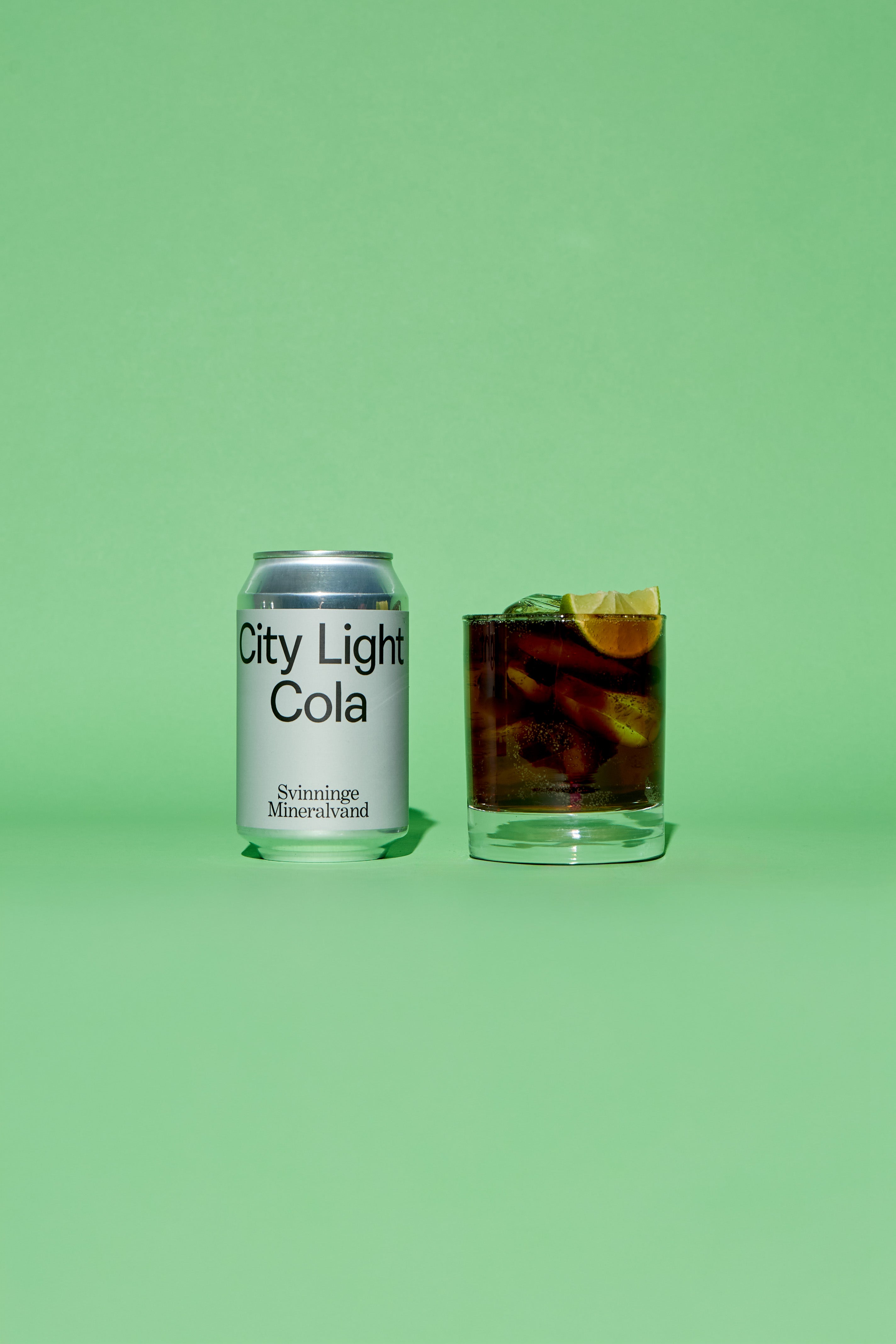 City Light Cola silver grey can and glass with drink on a green background
