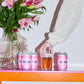 Three cans of To Øl's Implosion Pink Sour beer on a table with a glass and a bouquet of pink flowers.