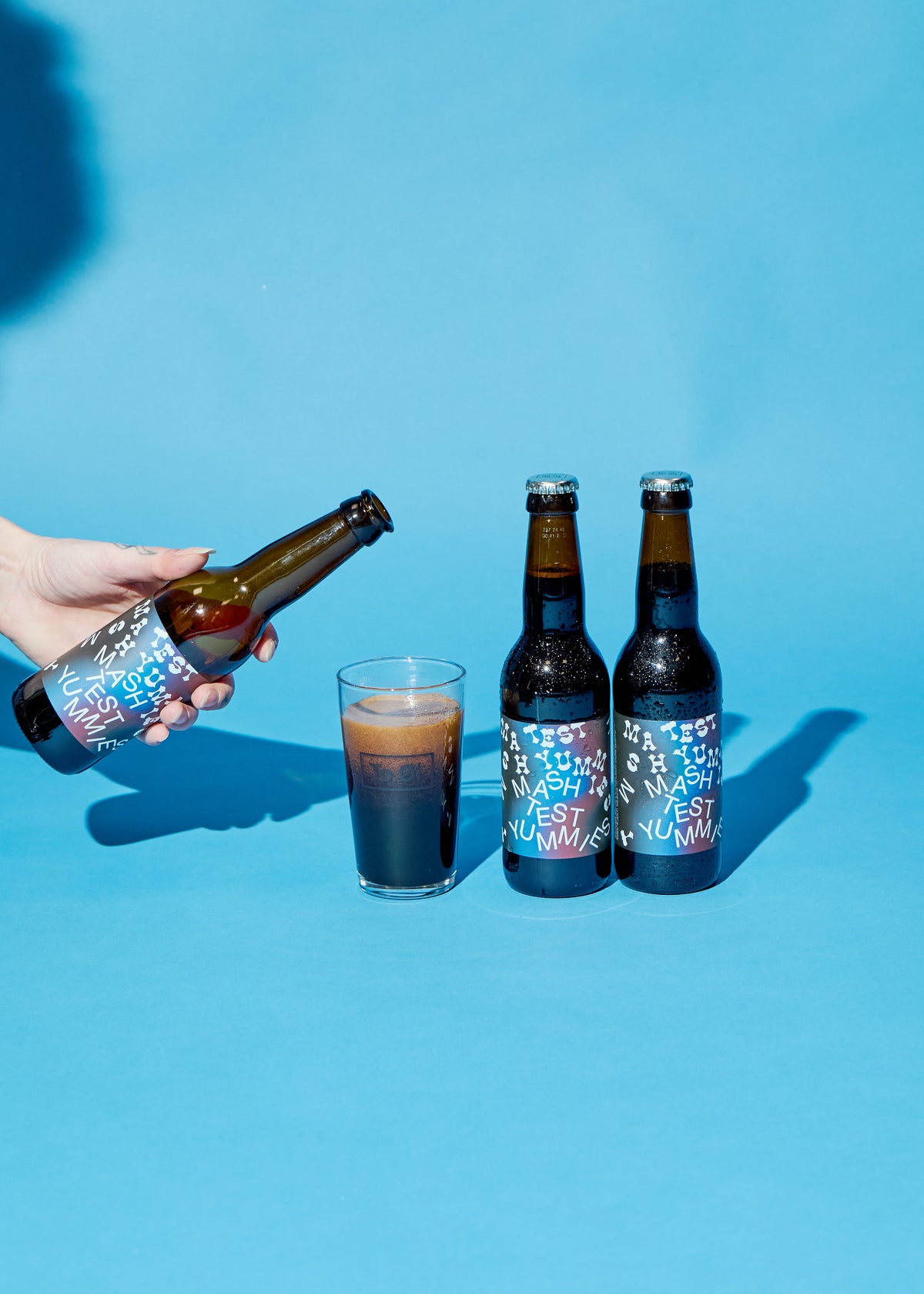 Two Mash Test Yummies bottles by To Øl featuring a poured beer glass placed on a blue background.