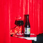 One bottle of Smoke On The Porter, Fire In The Rye - BA 2022 on a silver tray with a red glove holding a beer glass filled of the dark beer on a background with red curtains.