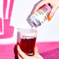 Person pouring a drink from a To Øl Berry Barrage can into a glass with a pink background.