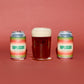 Two aluminum cans of To:01 Implosion beer flanked by a glass of dark amber beer with a thick white head, set against a solid terracotta background.