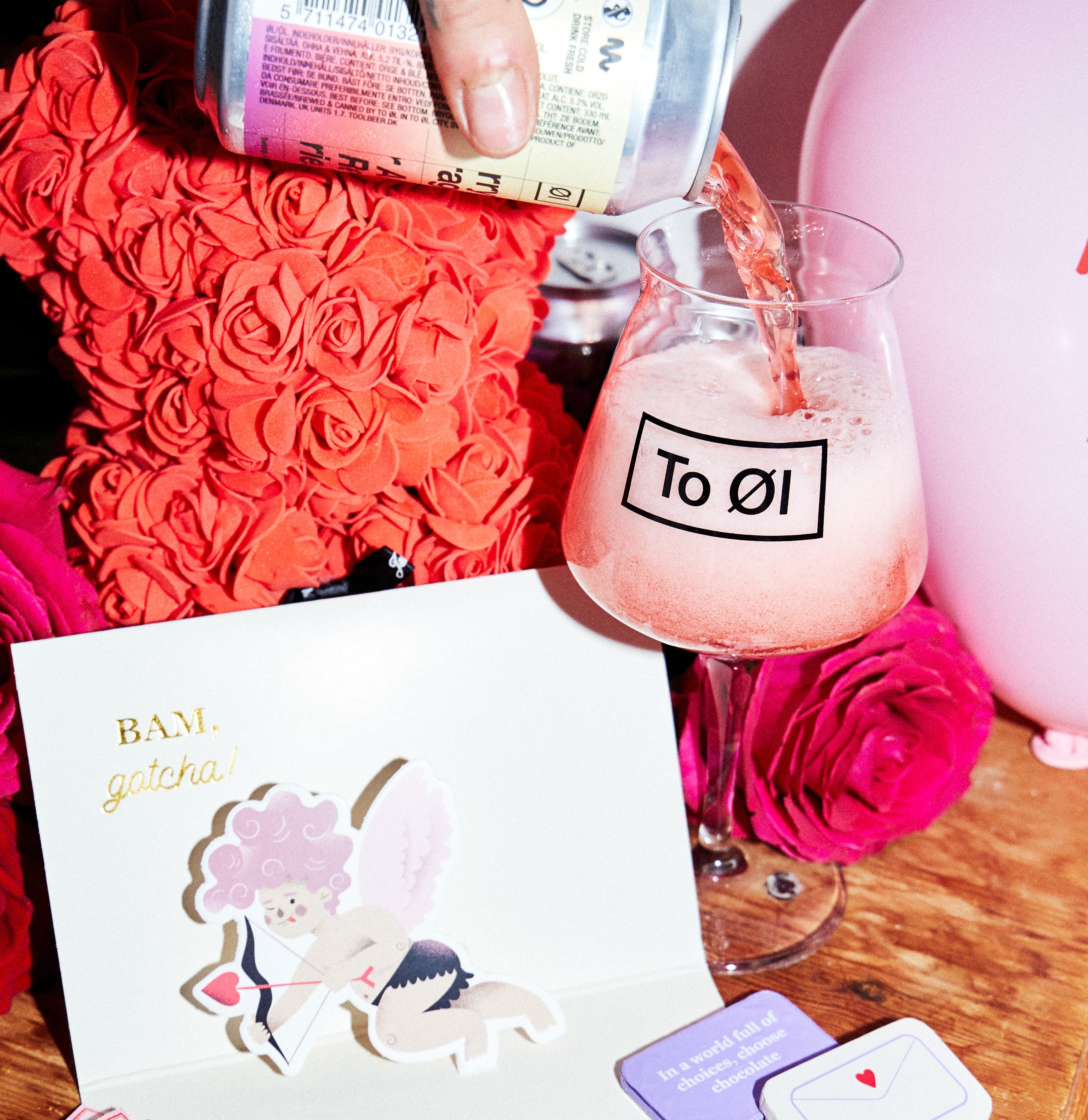 Valentine's Day card with pink roses and a glass of pink drink on a wooden table.
