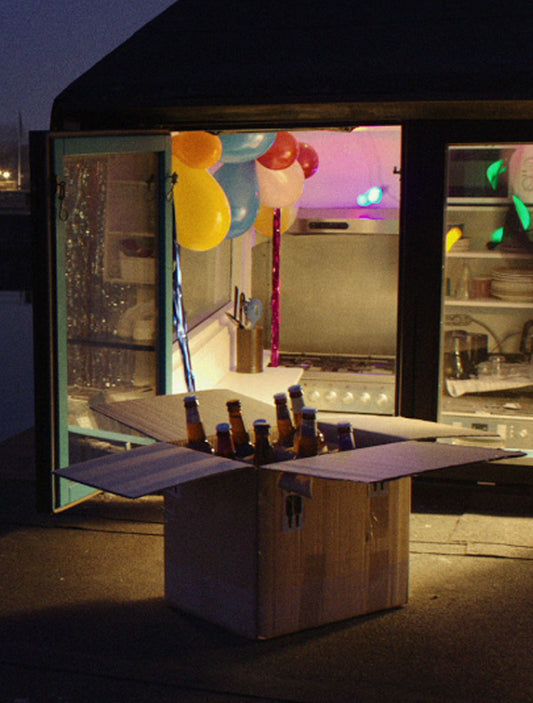 A gift box containing various bottles of dark beer displayed in a window with colorful lights.