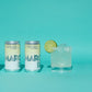 Two cans of Mikropolis Margaritas on a turquoise background with a glass of margarita and lime.